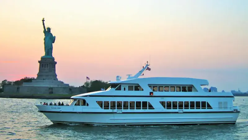 White party yacht cruising past the Statue of Liberty at sunset on the New York harbor