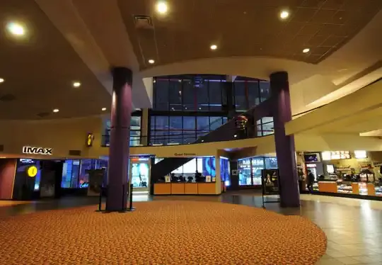 Movie theater lobby with tall columns, patterned carpet, IMAX entrance and concession counters under recessed lighting