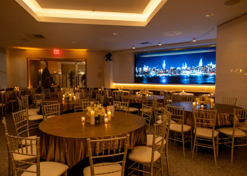 Banquet room set with gold-draped round tables, candles and flowers under a lit NYC skyline mural