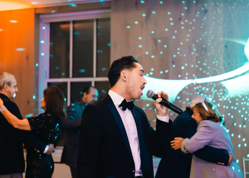 Singer in a tuxedo with a microphone as couples dance under blue starry lighting at a New Year's Eve gala