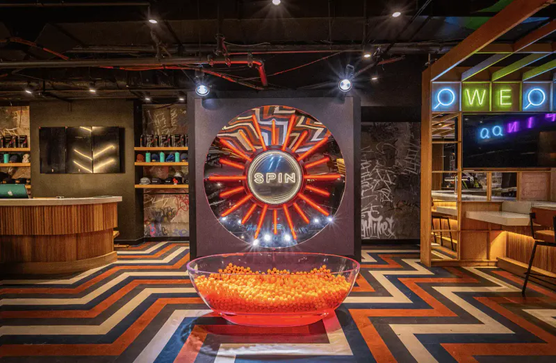 Entrance lobby at Spin NYC Times Square with neon Spin wheel, bowl of orange ping pong balls and chevron floor