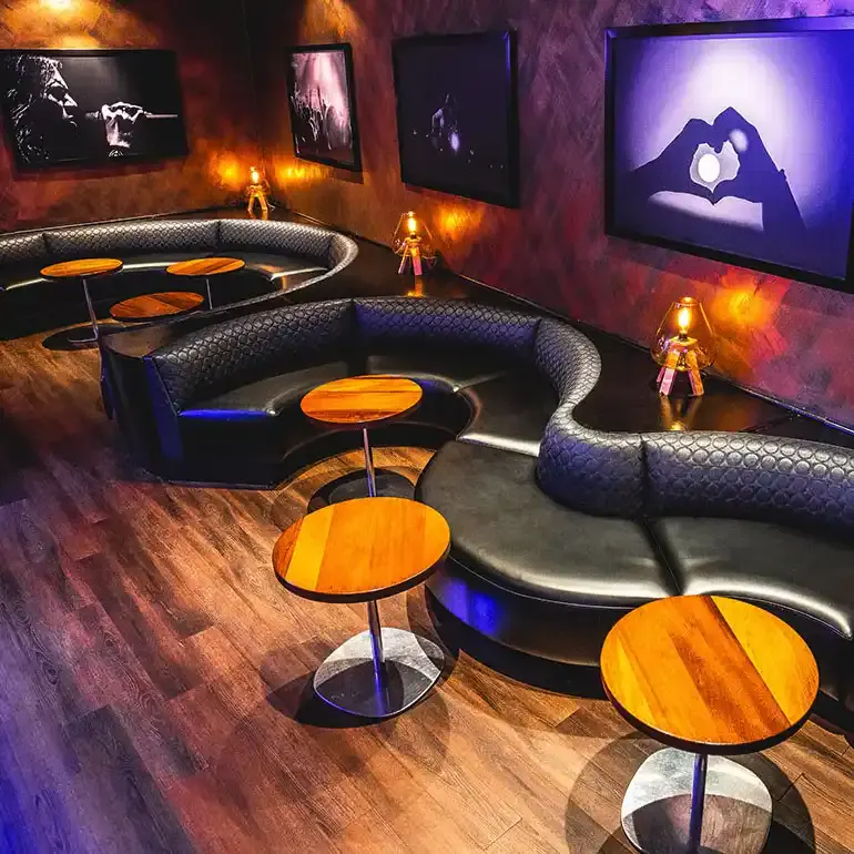 Curved black leather banquettes and round wood tables in a purple-lit lounge with wall screens at Frames in Times Square