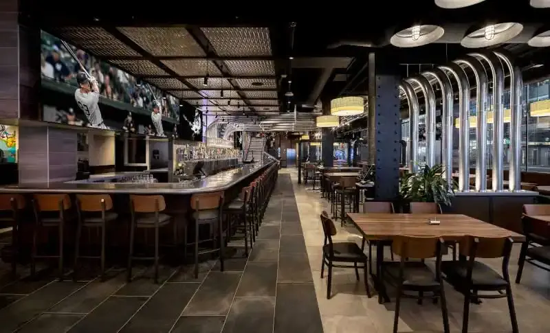 Long bar with stools and big screens showing baseball inside Yard House Times Square, with wood dining tables