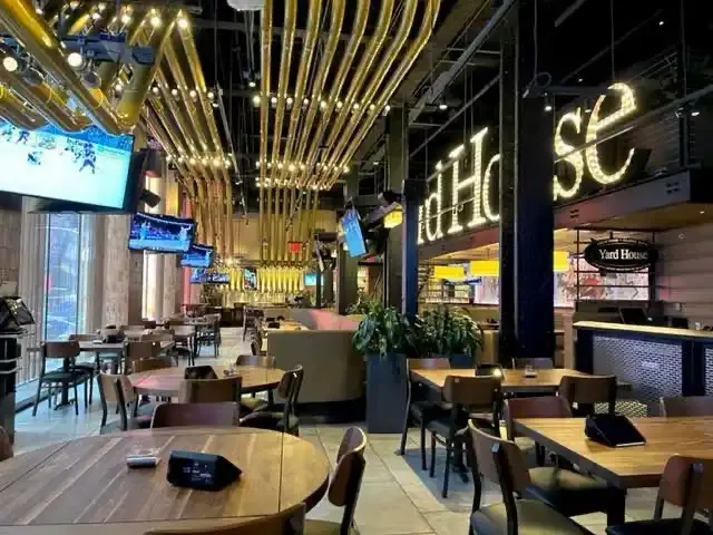 Interior of Yard House Times Square with wooden tables, TV screens and glowing marquee lettering above the bar