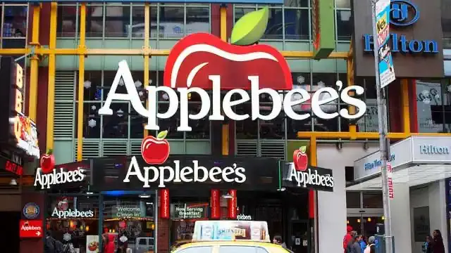 Exterior of Applebee's on 42nd Street in Times Square with large apple signs, Hilton sign and a yellow taxi below