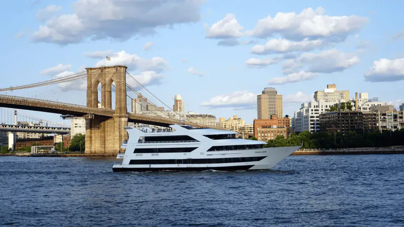 Timeless NYC yacht cruising the East River past the Brooklyn Bridge and skyline under a partly cloudy sky
