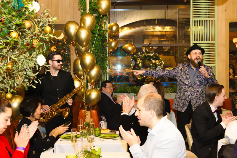 Singer with microphone and saxophonist performing for applauding guests at a New Year's Eve dinner gala with gold balloons