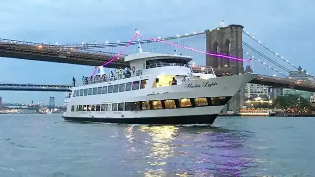 Harbor Lights party cruise yacht passing under the Brooklyn Bridge at dusk with guests on the open top deck