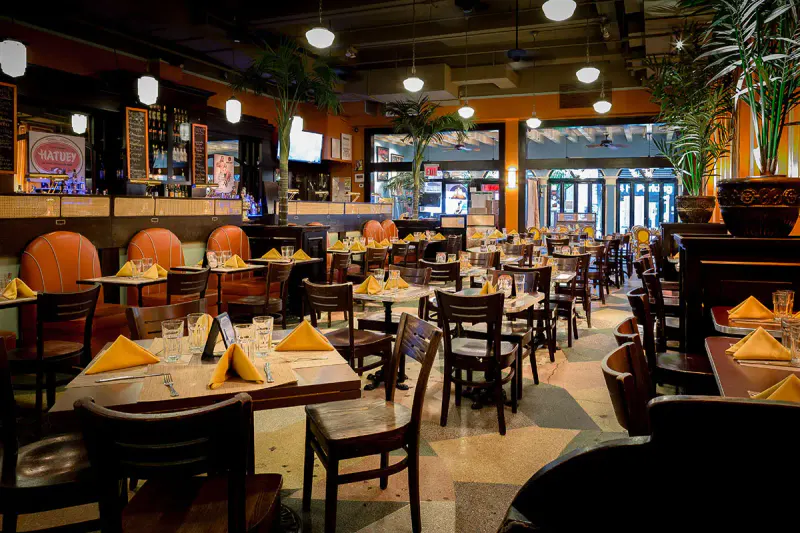Havana Central dining room with yellow napkins on set tables, leather booths, bar and palm trees