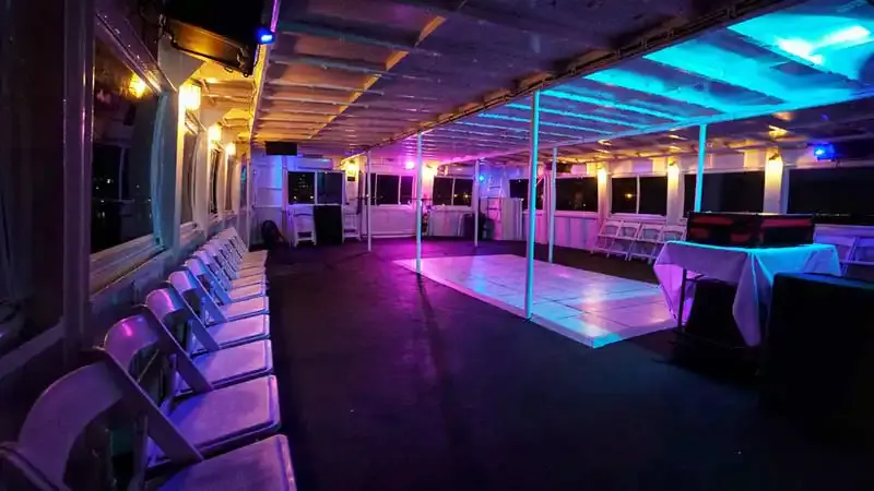 Empty yacht deck on a party cruise with a lit dance floor, white chairs and purple and blue lighting