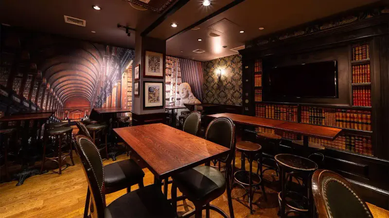 Library-themed back room at The Long Room NYC with wood tables, bar stools, bookshelves and a wall mural
