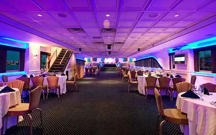 Interior dining deck of the Atlantis yacht with set tables, purple and blue lighting and a dance floor at the far end