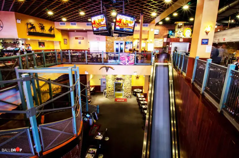 Two-level interior of Dallas BBQ Times Square with escalator, balcony railings, TV screens and dining tables below