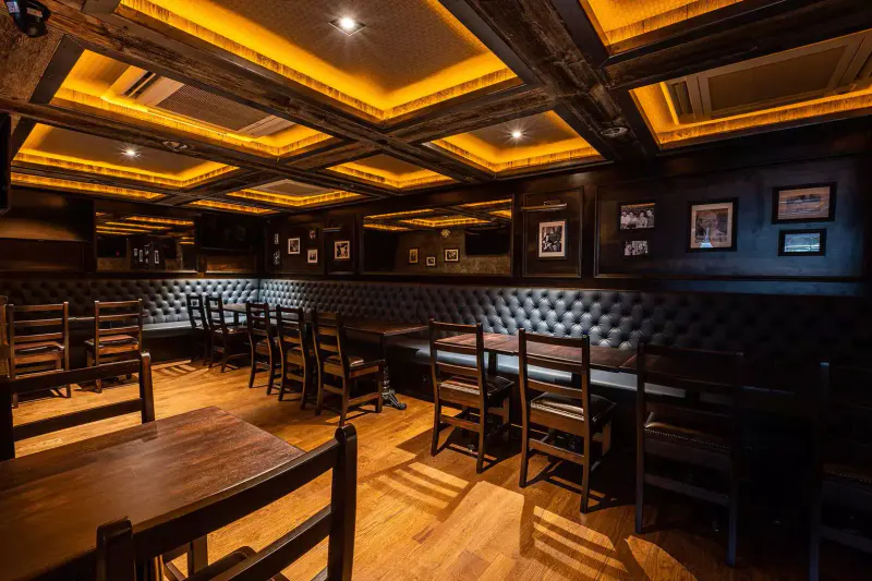 Dark wood dining room at Stout NYC Bryant Park with leather booths, wooden tables and warm coffered ceiling lighting