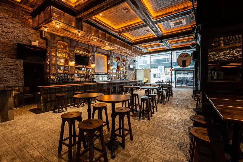 Interior of Stout NYC Bryant Park with wooden high-top tables, stools, long bar and warm ceiling lighting