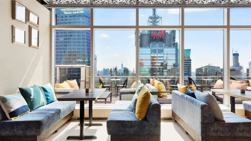 Sunlit rooftop lounge at Hyatt Centric Times Square with cushioned banquettes and floor-to-ceiling windows over the skyline