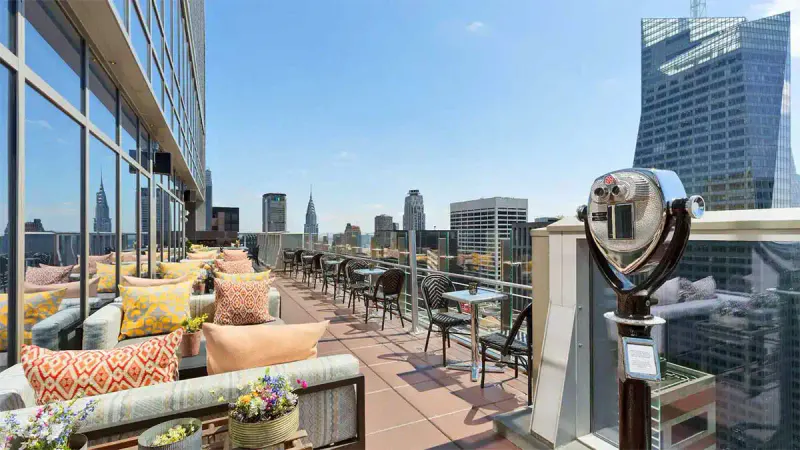 Rooftop terrace at Hyatt Centric Times Square with cushioned lounge seating, viewing scope and Manhattan skyline views