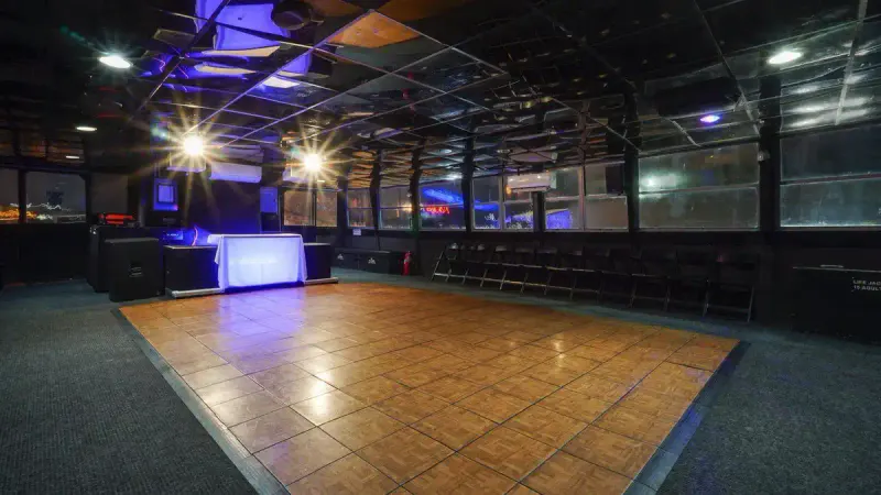 Empty wood dance floor and DJ booth on an enclosed yacht deck with windows and chairs along the wall