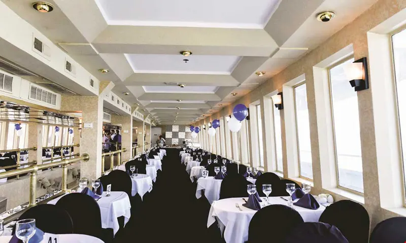 Dining deck on the Cornucopia Princess party cruise with white-clothed tables, numbered seating and blue balloons by the