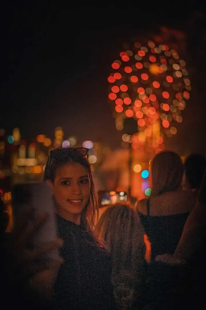 Smiling guest on the boat deck as red July 4th fireworks burst over the city skyline at night