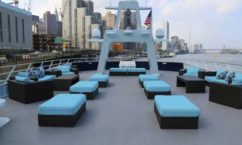 Open top deck of the Atlantis Yacht with turquoise lounge seating, American flag and Manhattan skyline behind