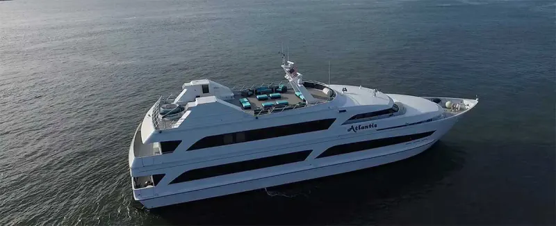 Aerial view of the white Atlantis yacht cruising on open water with an open-air top deck