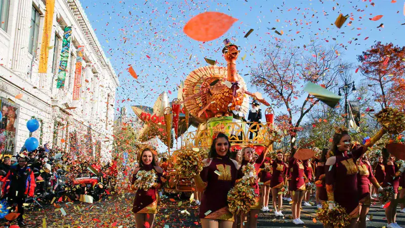 Thanksgiving parade turkey float and dancers with pom-poms marching through falling confetti on a sunny NYC street
