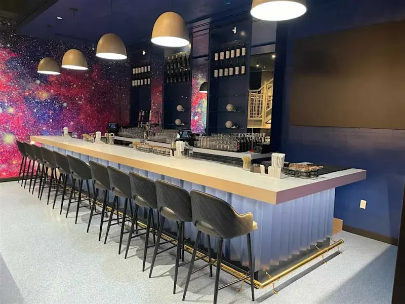 Long bar with black barstools, dome pendant lights and a galaxy mural at Planet Hollywood Times Square