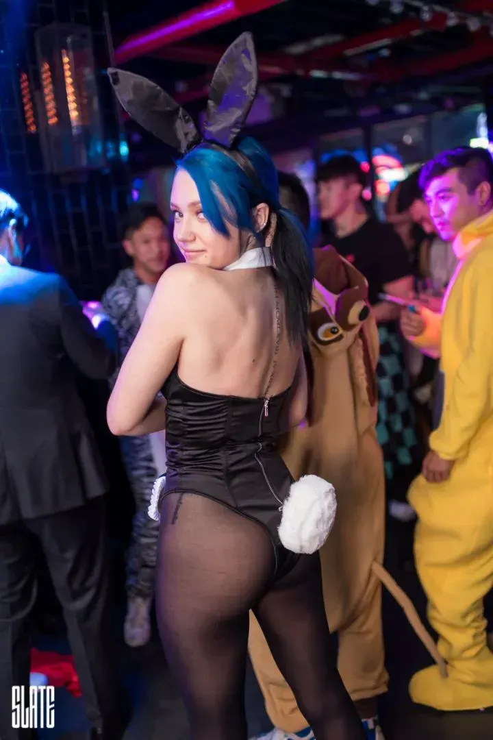 Guest in a black bunny costume with blue hair looking back on the crowded dance floor at a Halloween party at Slate NY