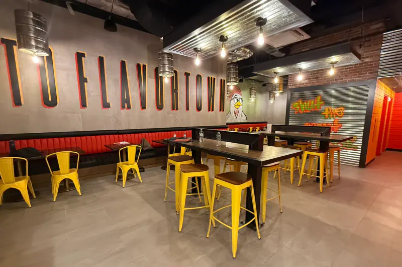 Dining room at Chicken Guy Times Square with yellow stools, high tables, red banquettes and Flavortown wall lettering