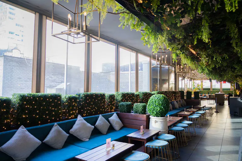Rooftop lounge at Elsie Rooftop with blue banquettes, hedge walls with string lights, greenery ceiling and city windows