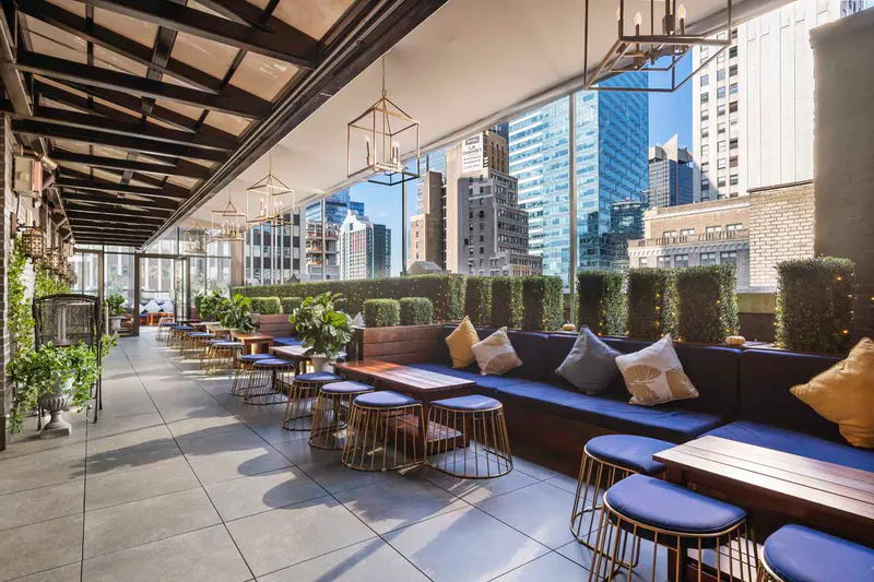 Elsie Rooftop terrace with blue banquette seating, hedges and lantern lights overlooking the Midtown skyline