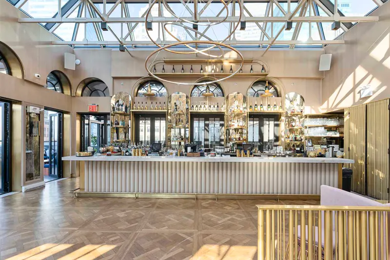 Marble bar with gold ring chandelier and glass skylight ceiling at Elsie Rooftop in NYC