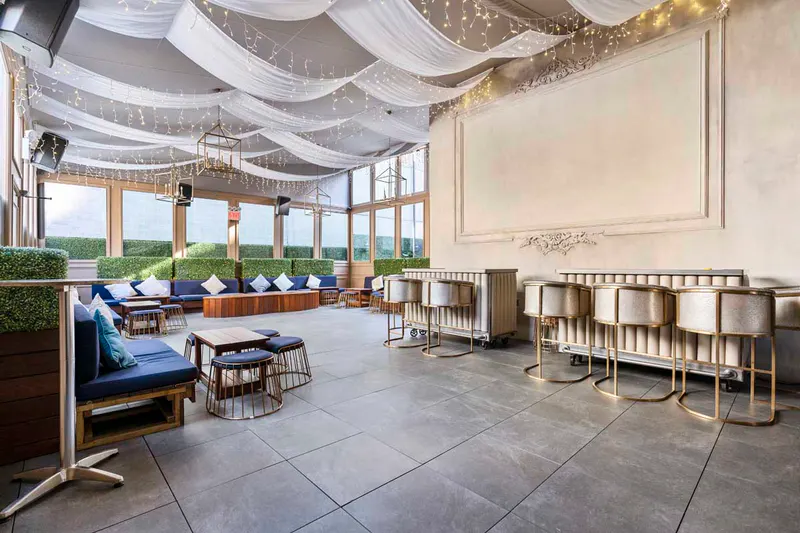 Rooftop lounge at Elsie Rooftop with draped ceiling, string lights, blue banquettes and gold bar stools
