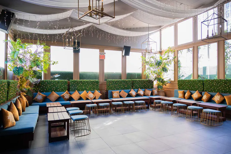 Elsie Rooftop lounge with blue banquettes, gold pillows, hedge walls, draped ceiling and string lights