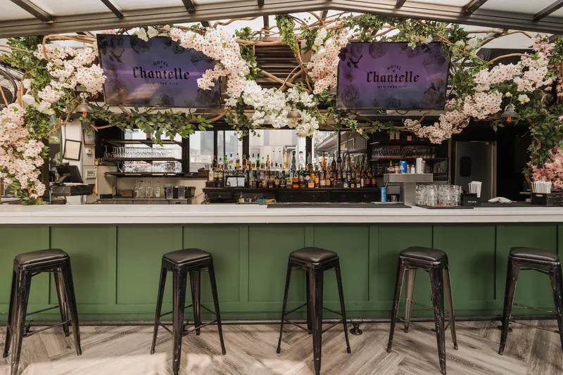 Rooftop bar at Hotel Chantelle with green bar front, black stools, floral vines and screens with the venue name