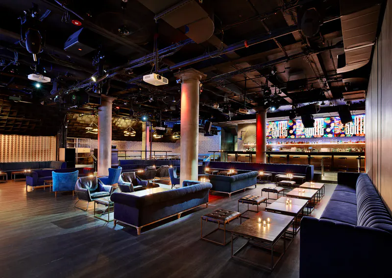 Interior of Slate NY with blue velvet couches, low candlelit tables, columns and a lit bar at the back