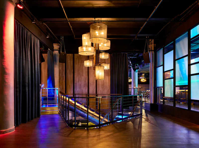 Upper level at Slate NY with drum chandeliers, staircase railing, velvet curtains and glowing video screens