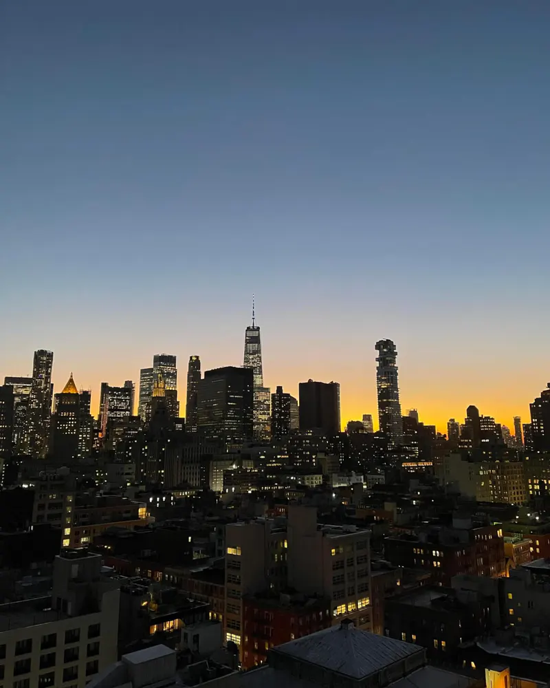 Rooftop view of the Lower Manhattan skyline at dusk with orange sunset glow behind the towers