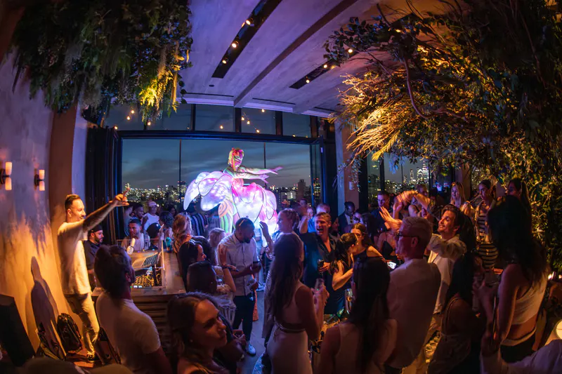 Crowded indoor rooftop party at The Highlight Room with a costumed light-up performer and city skyline through the windows