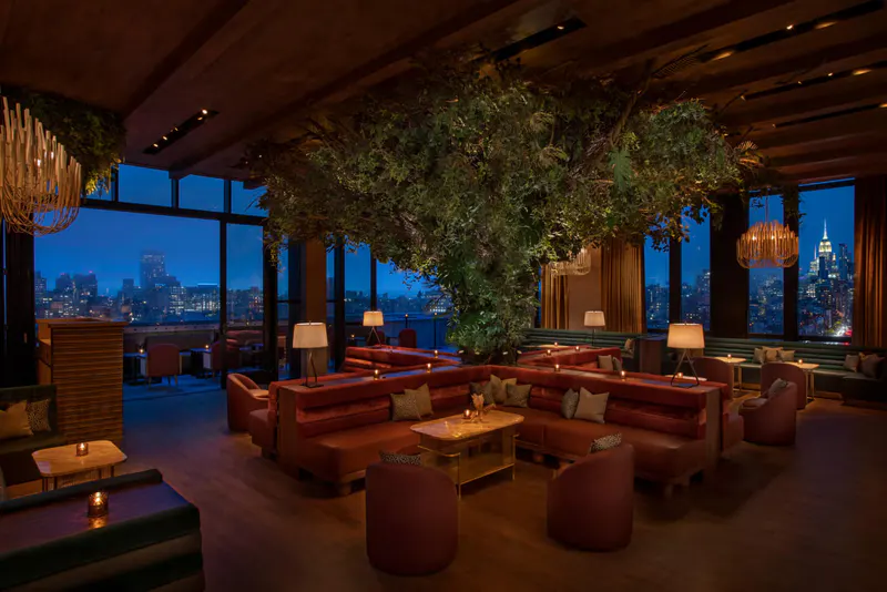 Rooftop lounge at The Highlight Room with velvet sofas, hanging greenery and floor-to-ceiling windows over the NYC skyline at