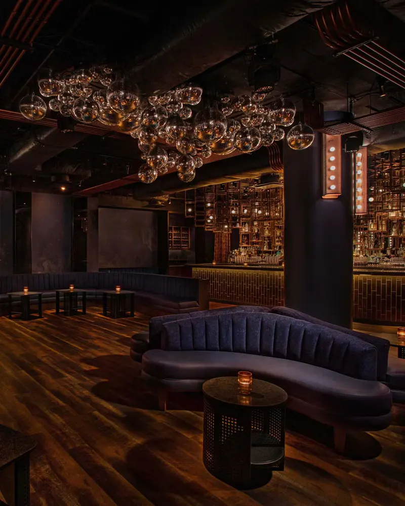 Dimly lit lounge at Loosies Nightclub with curved velvet sofas, bubble glass chandelier and backlit bar
